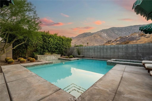 pool at dusk featuring a fenced backyard, a mountain view, an in ground hot tub, a fenced in pool, and a patio area