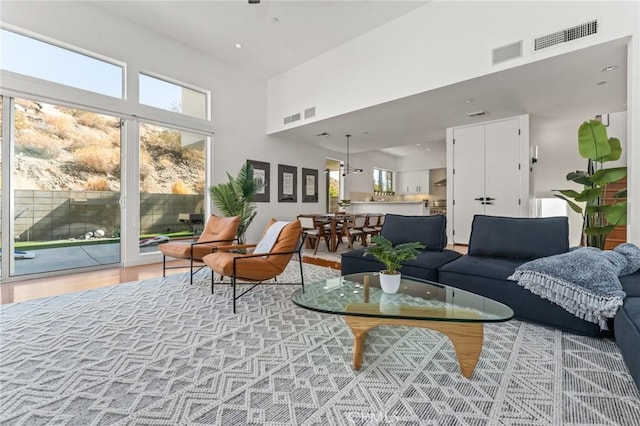 living room featuring a towering ceiling, light wood finished floors, and visible vents