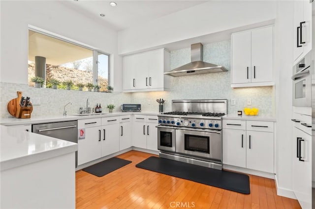 kitchen with appliances with stainless steel finishes, light countertops, white cabinetry, and wall chimney exhaust hood