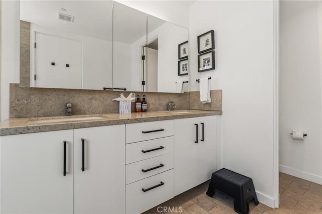 bathroom with double vanity, tasteful backsplash, baseboards, visible vents, and a sink