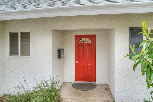 property entrance with roof with shingles and stucco siding