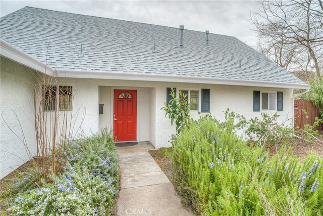 doorway to property with stucco siding, fence, and roof with shingles