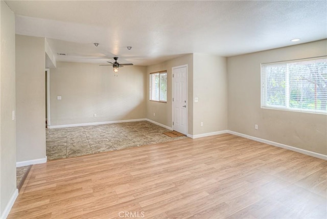 empty room with a ceiling fan, light wood-type flooring, a healthy amount of sunlight, and baseboards