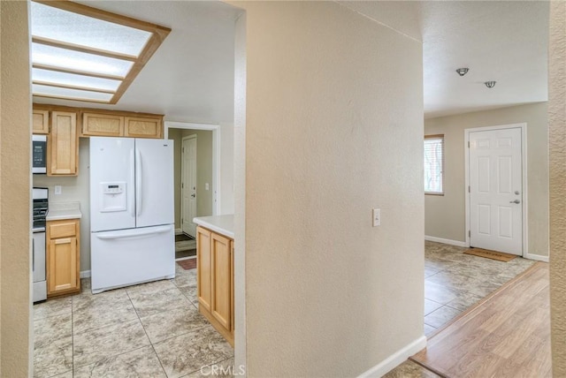 kitchen featuring light tile patterned floors, light countertops, stove, white fridge with ice dispenser, and baseboards