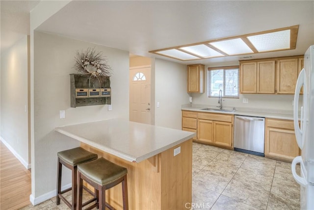 kitchen featuring stainless steel dishwasher, light brown cabinetry, freestanding refrigerator, a sink, and a peninsula