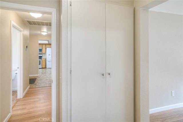 corridor featuring light wood finished floors, baseboards, and visible vents