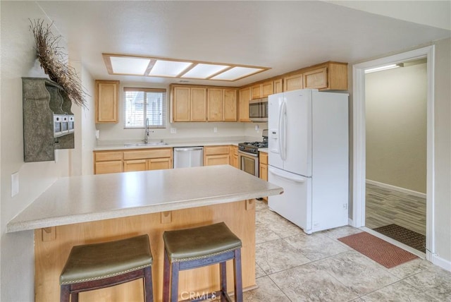 kitchen featuring stainless steel appliances, light brown cabinetry, a peninsula, and a sink