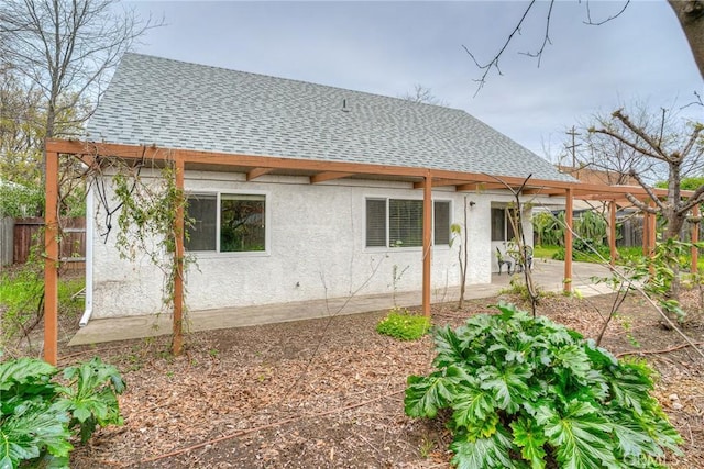 rear view of property featuring a patio, stucco siding, a shingled roof, fence, and a pergola