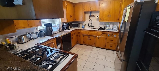 kitchen featuring backsplash, brown cabinetry, light tile patterned flooring, a sink, and black appliances