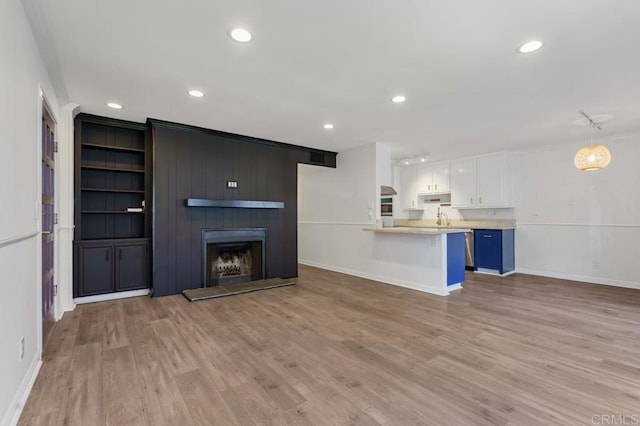 unfurnished living room with recessed lighting, a large fireplace, built in features, baseboards, and light wood-type flooring