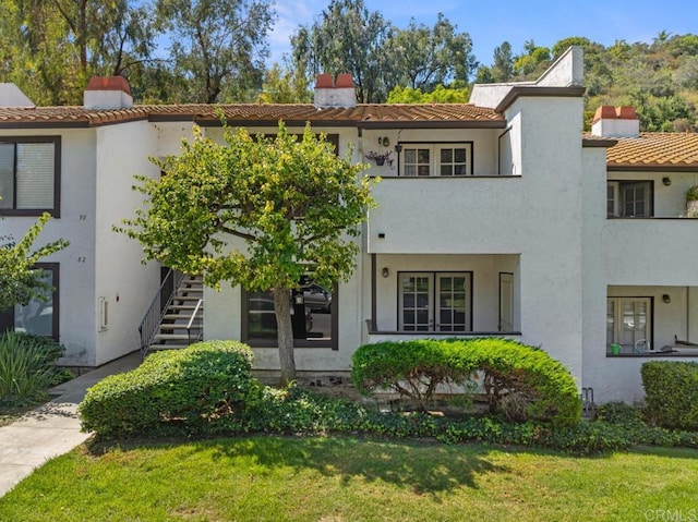 view of front of house featuring a chimney, stairway, a front yard, and stucco siding