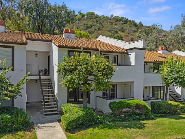 view of front facade featuring a chimney, a tile roof, stairway, and stucco siding