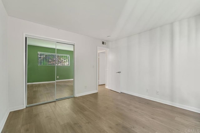 unfurnished bedroom featuring a closet, visible vents, baseboards, and wood finished floors