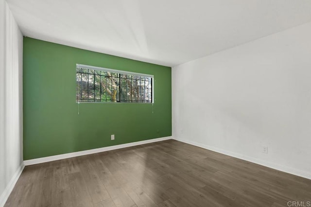 spare room featuring baseboards and dark wood finished floors