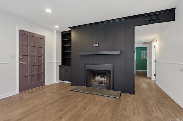 unfurnished living room with built in shelves, a fireplace, baseboards, and wood finished floors