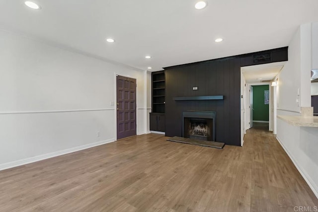 unfurnished living room featuring recessed lighting, a large fireplace, baseboards, and wood finished floors