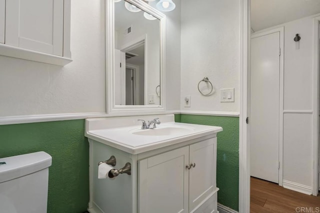 bathroom with a textured wall, toilet, wood finished floors, vanity, and visible vents