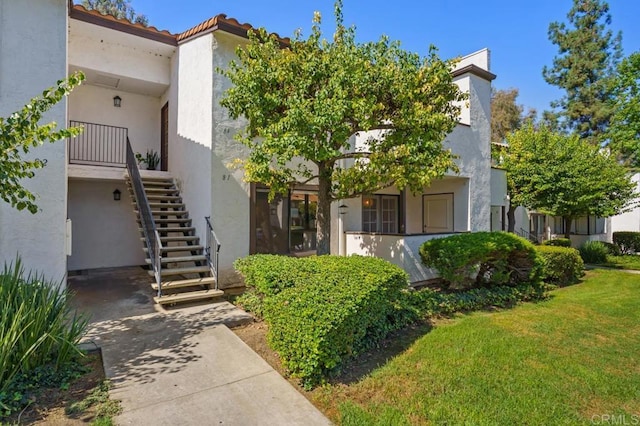 exterior space with a tile roof, stairs, a front lawn, and stucco siding