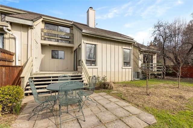 rear view of property with a balcony, fence, outdoor dining space, a chimney, and a patio area