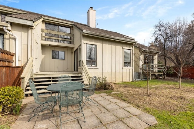 back of property featuring board and batten siding, a patio, a wooden deck, a chimney, and outdoor dining area