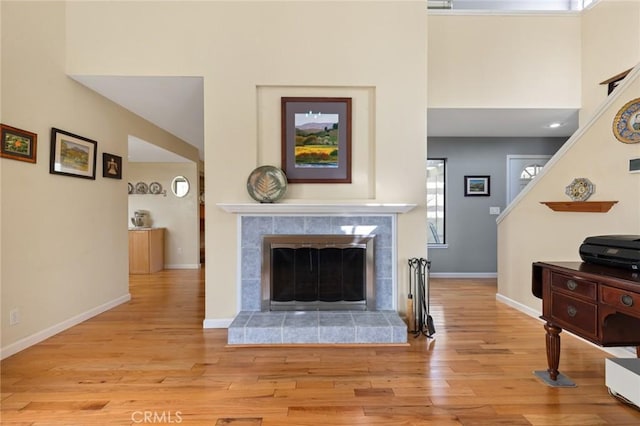 living room with light wood finished floors, stairway, a towering ceiling, a tiled fireplace, and baseboards