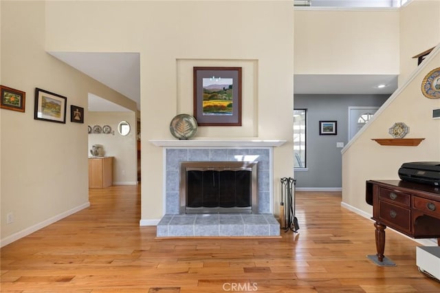 living area featuring baseboards, wood finished floors, a tile fireplace, and a high ceiling