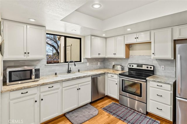 kitchen with light wood-style flooring, decorative backsplash, appliances with stainless steel finishes, white cabinetry, and a sink