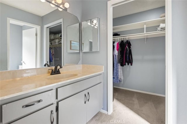 bathroom with a spacious closet, vanity, and baseboards