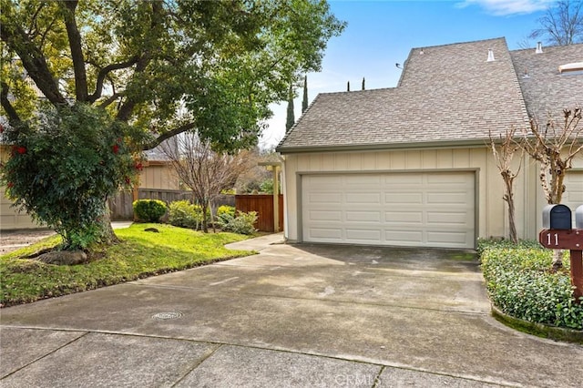 exterior space with a garage, fence, concrete driveway, and roof with shingles