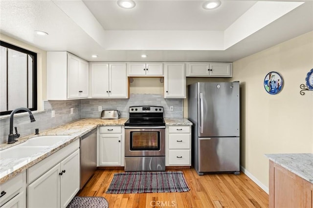 kitchen with a sink, white cabinets, appliances with stainless steel finishes, light wood-type flooring, and light stone countertops