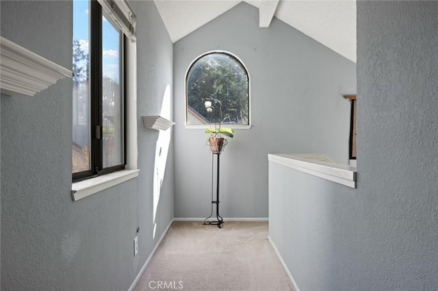 hallway featuring a textured wall, lofted ceiling with beams, carpet flooring, and baseboards