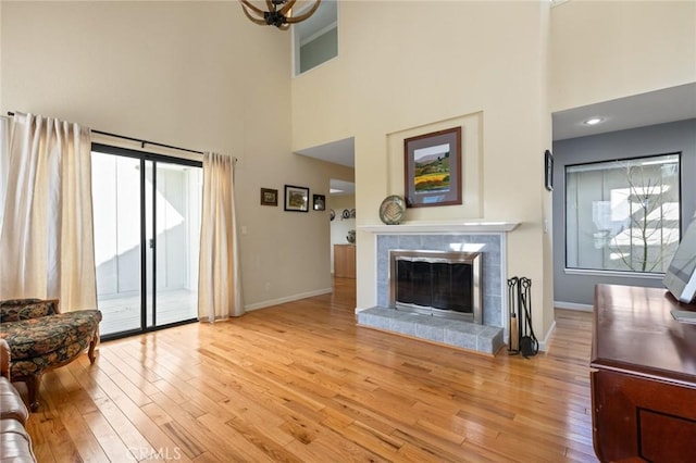 living room featuring a tiled fireplace, light wood-style flooring, and baseboards