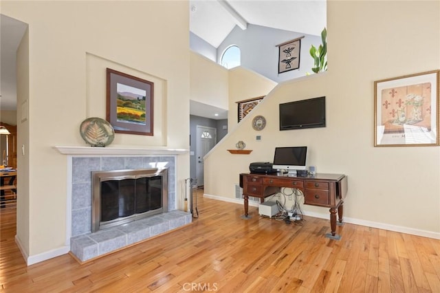 office space featuring wood finished floors, a tile fireplace, beamed ceiling, baseboards, and high vaulted ceiling