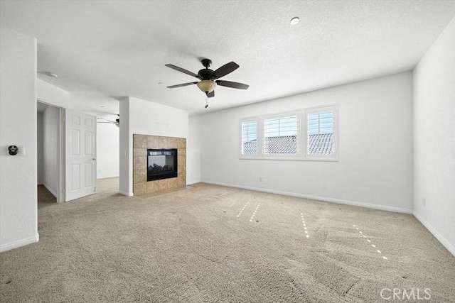 unfurnished living room featuring ceiling fan, a textured ceiling, light carpet, a fireplace, and baseboards