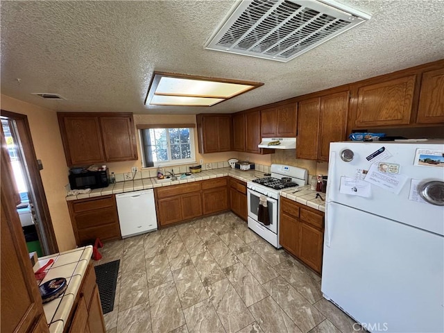 7687 Chase Ave, Hesperia, CA 92345 - kitchen featuring tile counters, under cabinet range hood, brown cabinetry, white appliances, and a textured ceiling