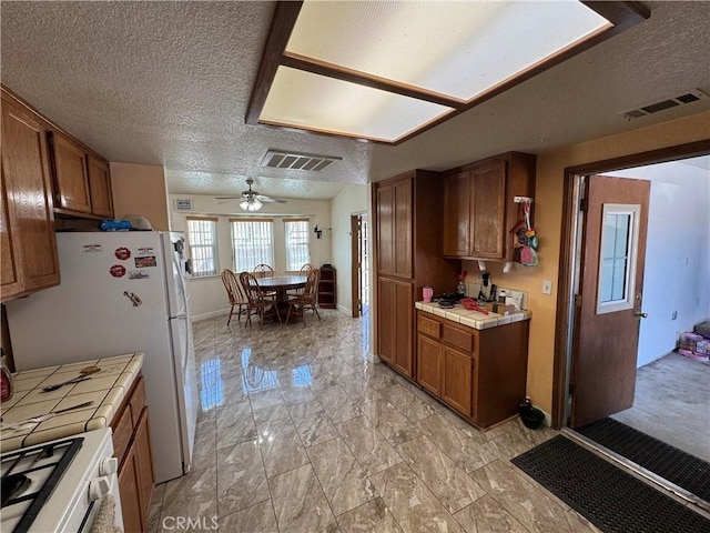 7687 Chase Ave, Hesperia, CA 92345 - kitchen with visible vents, a textured ceiling, tile counters, and brown cabinetry