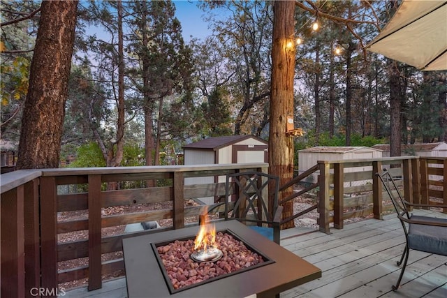 wooden terrace with a storage shed, an outdoor fire pit, and an outbuilding