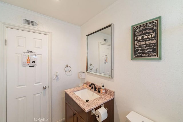 half bathroom with toilet, ornamental molding, vanity, and visible vents