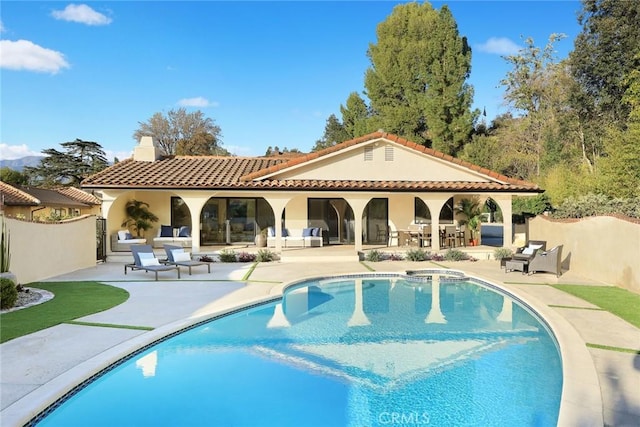 back of house featuring a pool with connected hot tub, a patio, a chimney, and fence