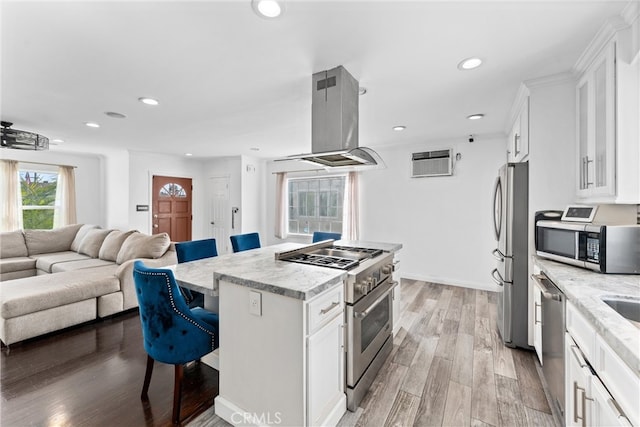 kitchen with island exhaust hood, stainless steel appliances, white cabinets, a kitchen island, and a kitchen bar