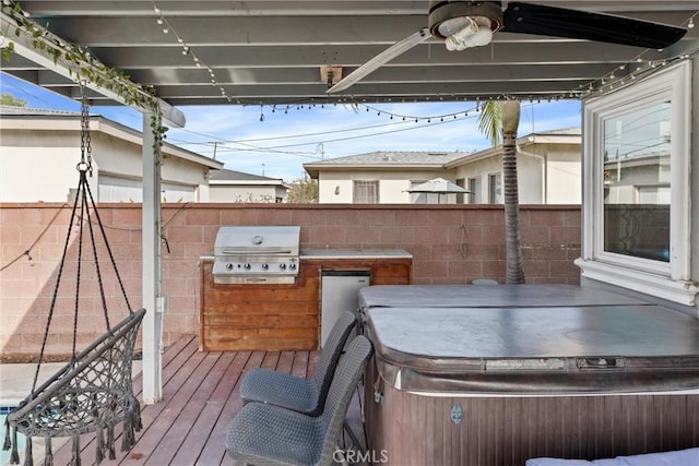 wooden terrace with a hot tub, a grill, fence, and exterior kitchen