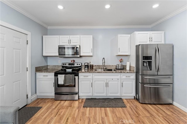 kitchen with stainless steel appliances, a sink, white cabinets, ornamental molding, and dark stone counters