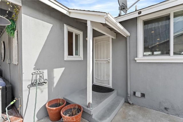 view of exterior entry with crawl space and stucco siding