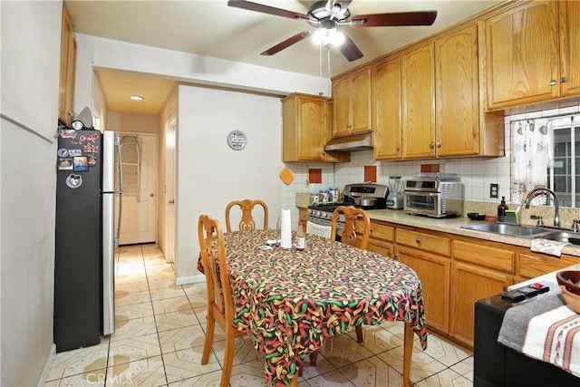 kitchen featuring a toaster, appliances with stainless steel finishes, a sink, under cabinet range hood, and backsplash