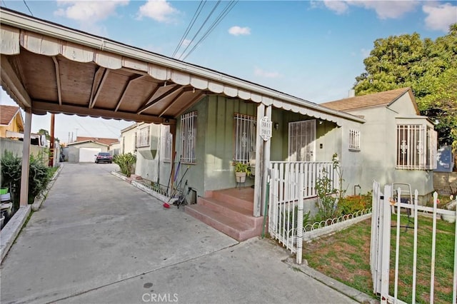 view of front facade with covered porch, fence, a carport, and an outbuilding