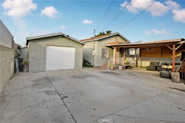 rear view of property featuring concrete driveway, a detached garage, fence, an outdoor structure, and stucco siding