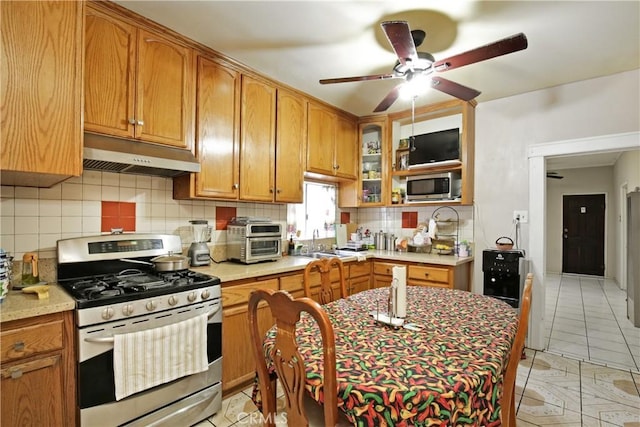 kitchen featuring a toaster, under cabinet range hood, stainless steel appliances, light countertops, and decorative backsplash