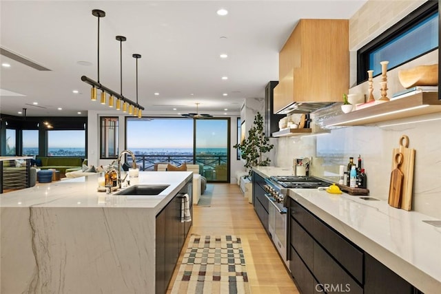 kitchen featuring decorative light fixtures, open floor plan, a sink, light stone countertops, and high end range