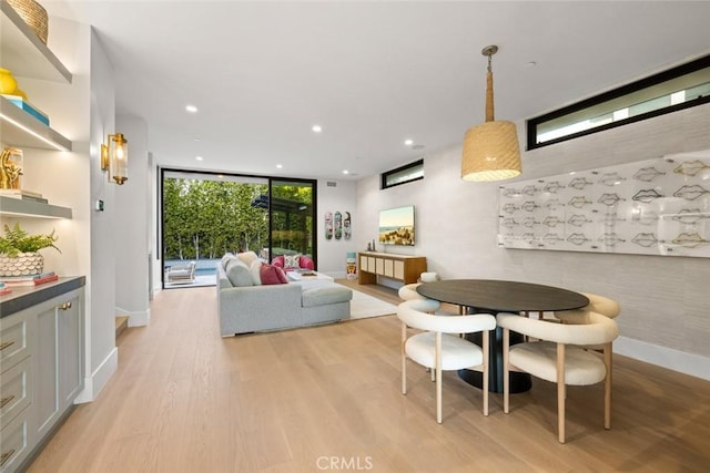 dining room featuring baseboards, light wood finished floors, a wall of windows, and recessed lighting