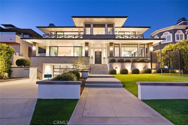 view of front of home featuring a trampoline, a front yard, a balcony, and stucco siding